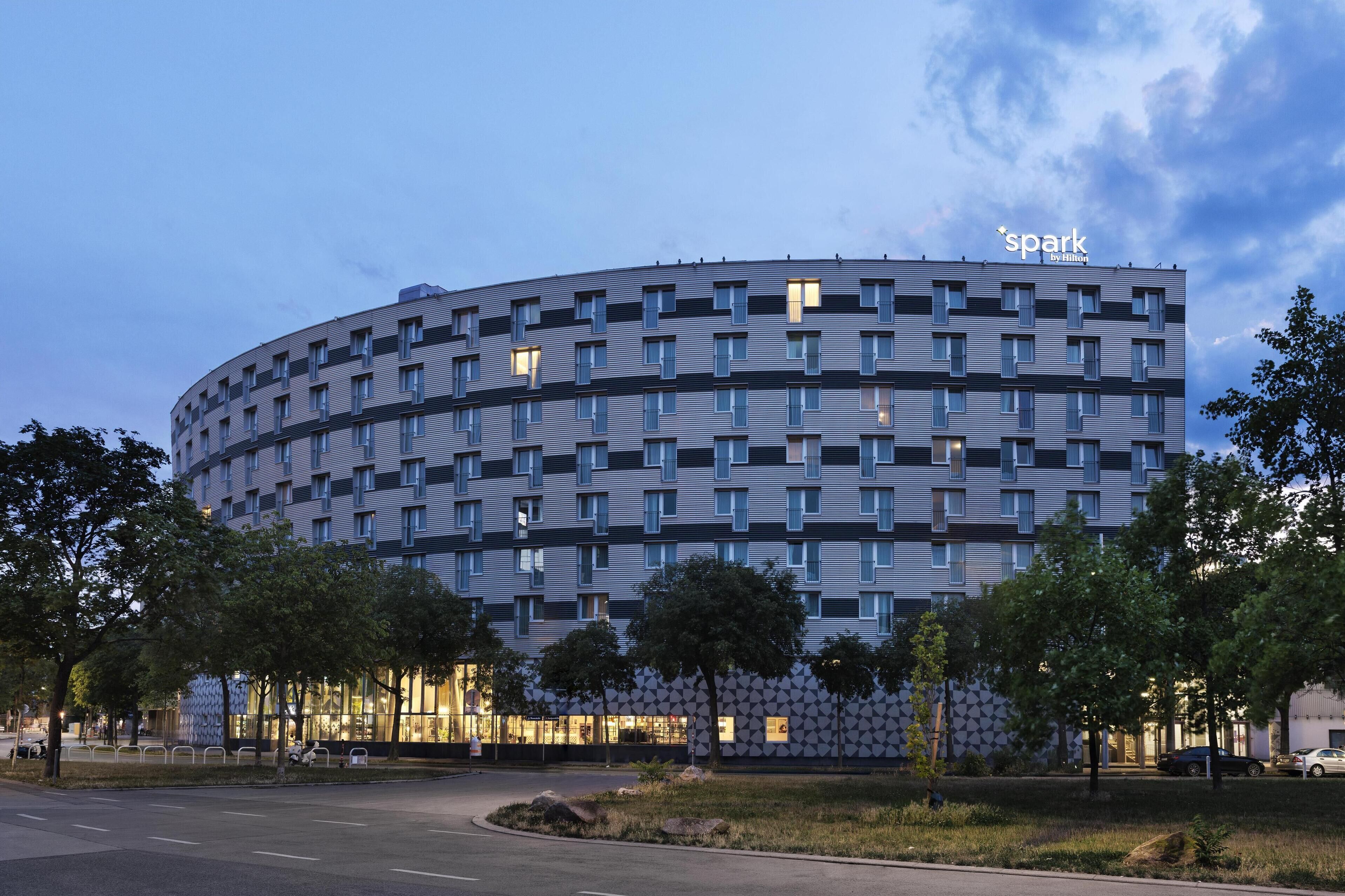 Um hotel moderno com fachada curva, várias janelas e uma placa com a inscrição "spark by Hilton".