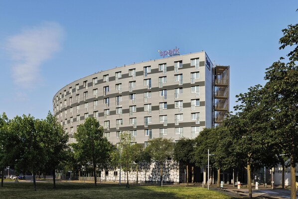A modern hotel with a curved facade, multiple floors, and a prominent sign on top. - Spark by Hilton Vienna Messe Prater (Vienna)