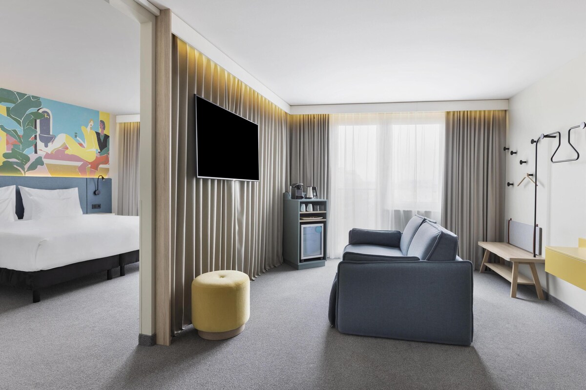 Een moderne hotelkamer met een bed, een bank, een televisie en een schilderij aan de muur.