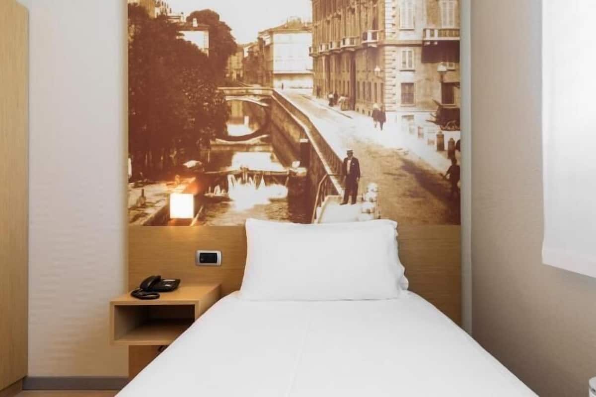 A hotel room with a bed, a nightstand with a phone, and a wall with a cityscape mural.