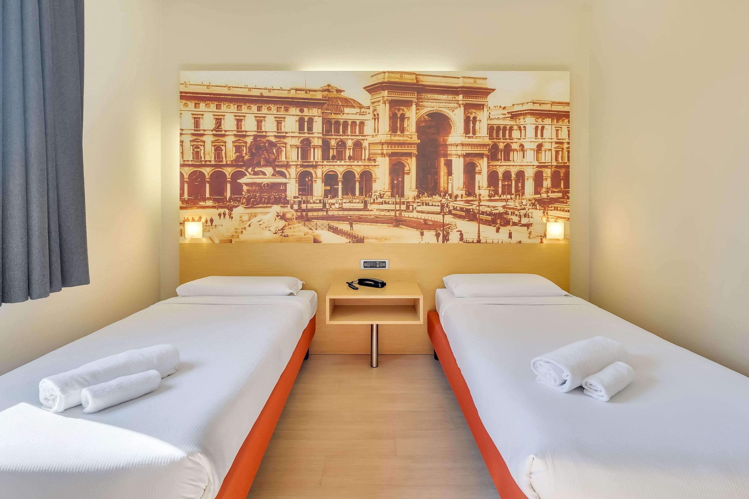 Ein Hotelzimmer mit zwei Betten, einem Nachttisch und einer großen Wandmalerei eines historischen Gebäudes.