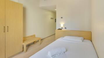 Une chambre d’hôtel avec un lit, une armoire en bois, un banc et une table de chevet avec un téléphone et une lampe.