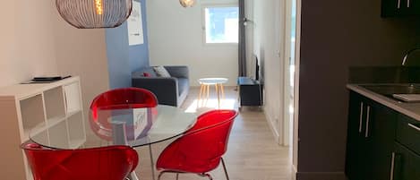 Una cocina moderna con comedor, que incluye una mesa de vidrio y sillas rojas, una lámpara colgante negra y vistas al salón.