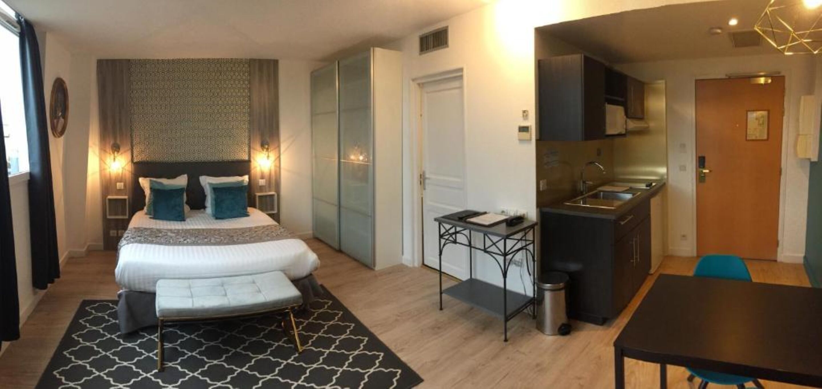 Een moderne hotelkamer met een groot bed, een kleine kitchenette, een zithoek en een aparte badkamer.