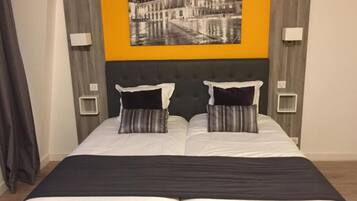 Una cama doble con dos almohadas, un cabecero oscuro y una amplia pintura en blanco y negro de un paisaje urbano.