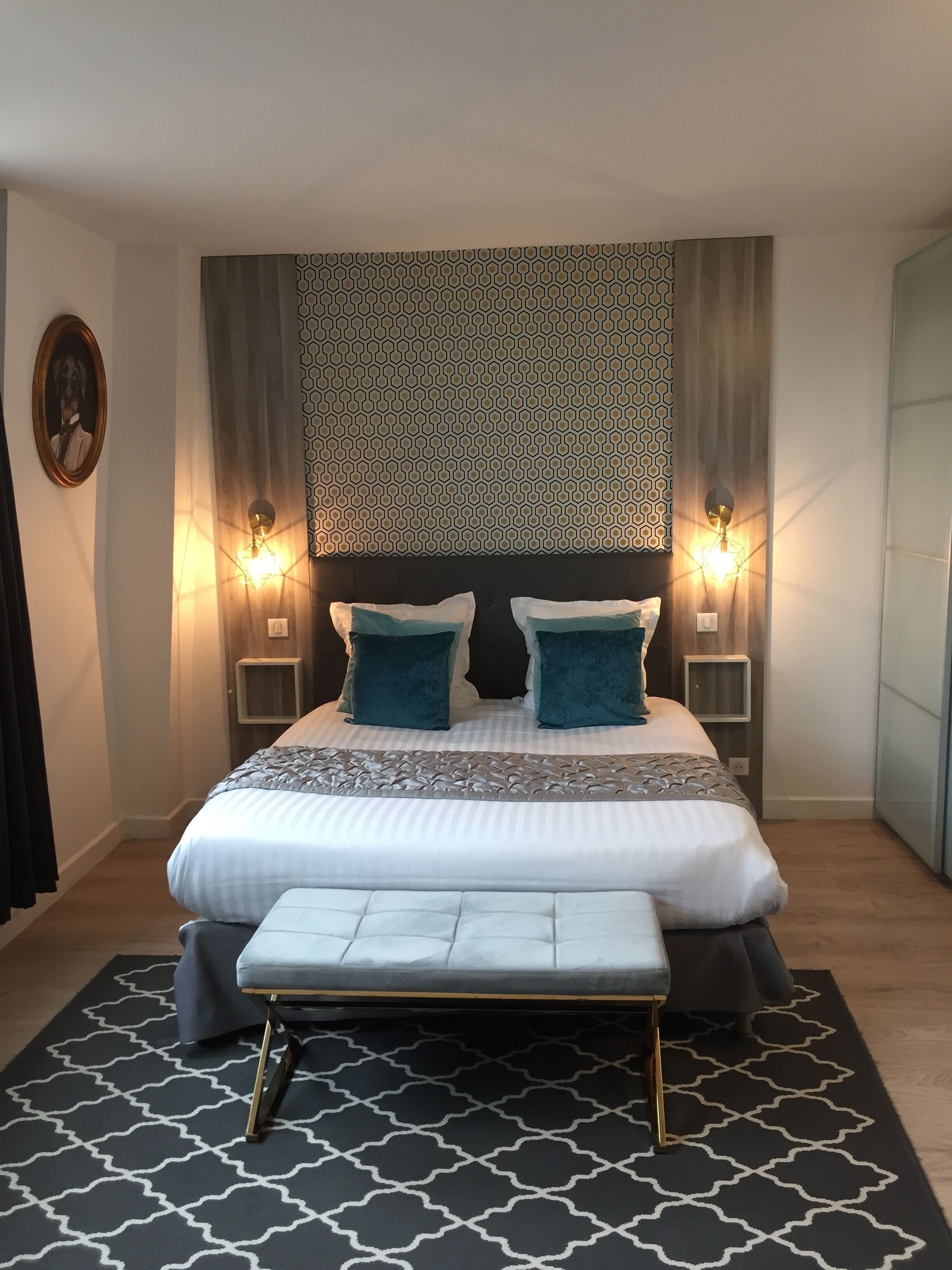 Een moderne slaapkamer met een groot bed, twee nachtkastjes, een bankje en decoratieve wand- en vloerpatronen.
