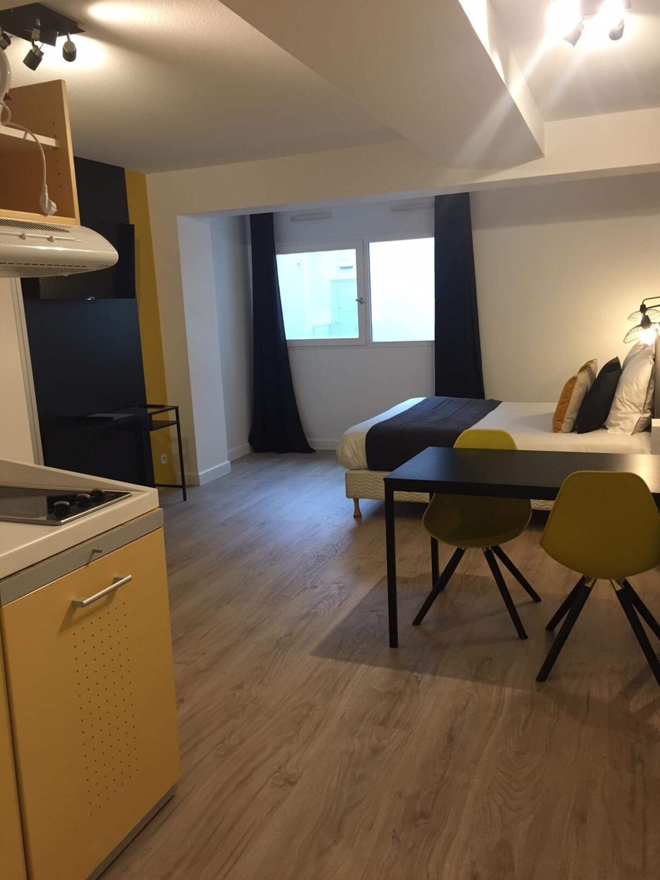 Una habitación pequeña con cama, una mesita y una kitchenette.