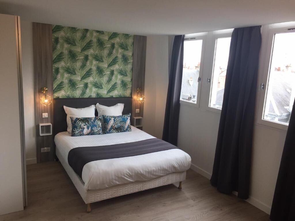 Un dormitorio con cama, pared decorada con motivos de hojas y ventana con cortinas.