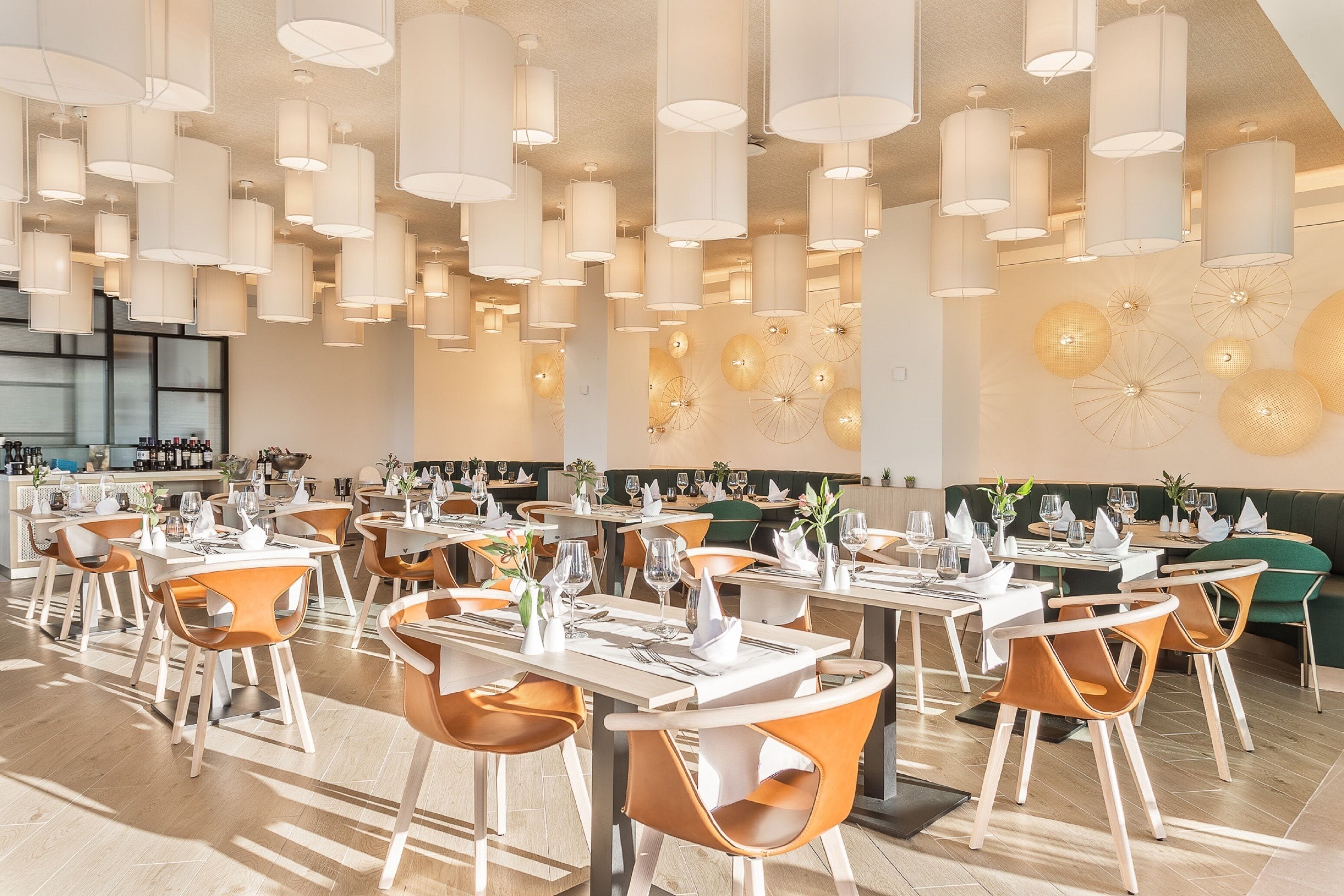 Ein geräumiges Restaurant mit mehreren Speisetischen, orangefarbenen Stühlen und Pendelleuchten.
