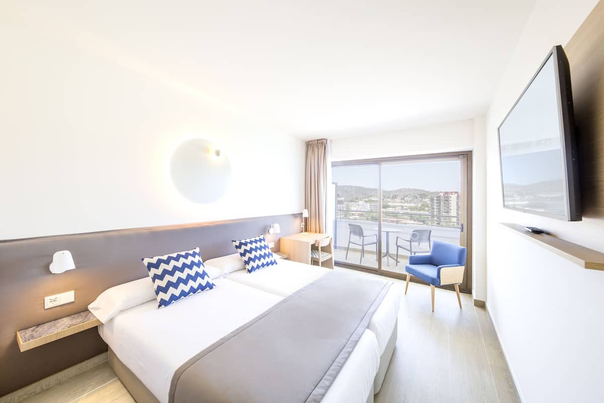 A hotel room with a bed, a desk, a chair, a TV, and a balcony with a view.
