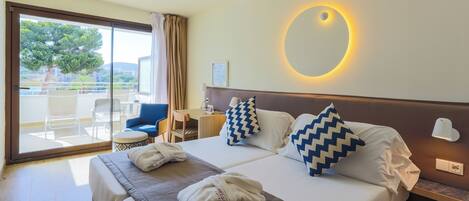 Habitación de hotel con cama, dos almohadas, mesita de noche con lámpara, una silla y vista al exterior.
