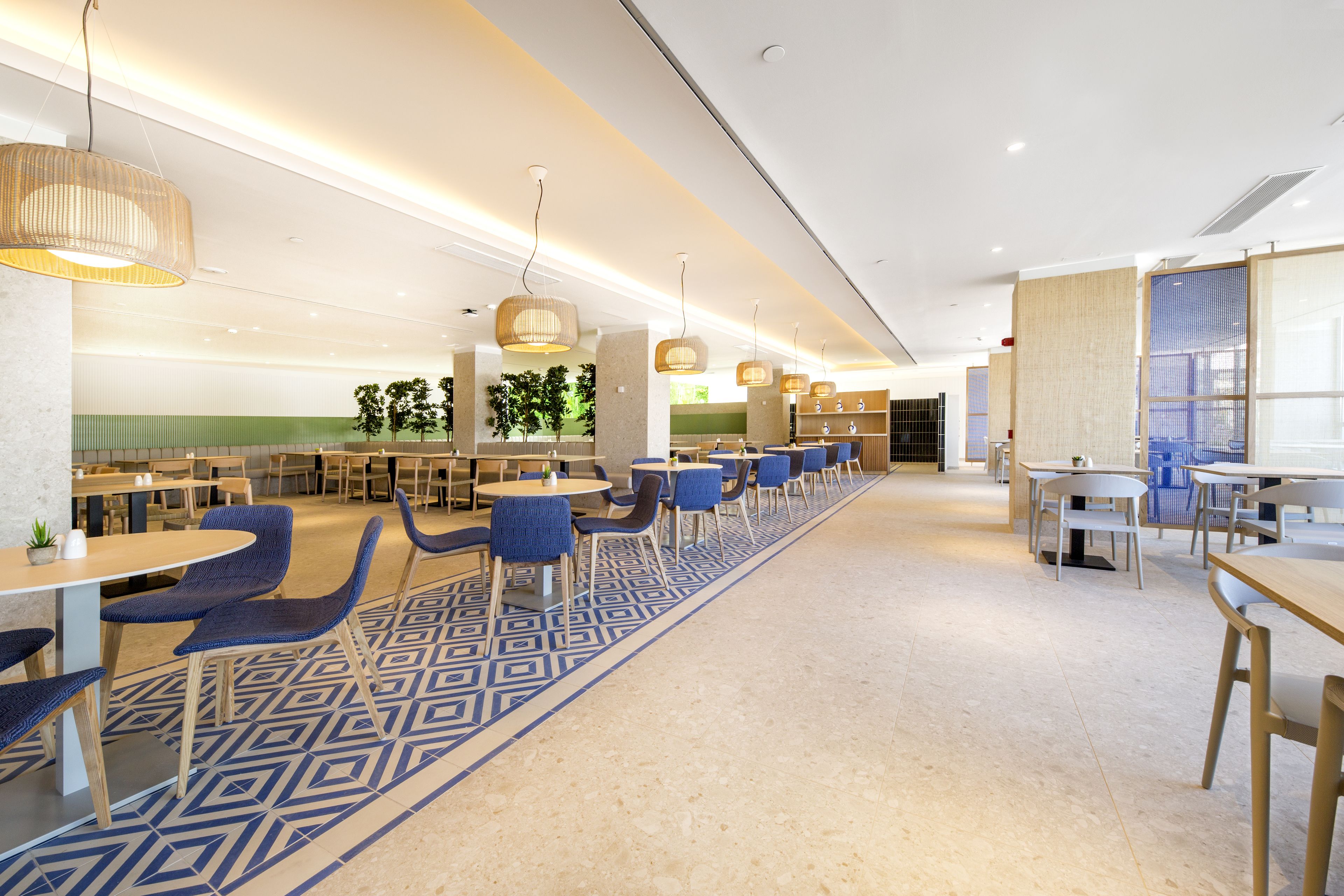 A modern dining area with multiple tables and chairs, a patterned carpet, and hanging pendant lights.