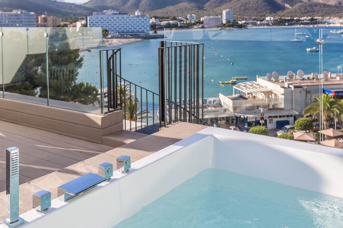 A rooftop pool with a glass balustrade, a bar area, and a view of the sea and buildings.