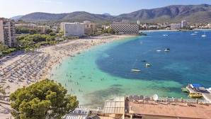 Un resort costero con playa, aguas turquesas cristalinas y montañas al fondo.