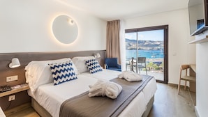 Habitación de hotel con cama, escritorio, silla, televisión y balcón con vista al mar.