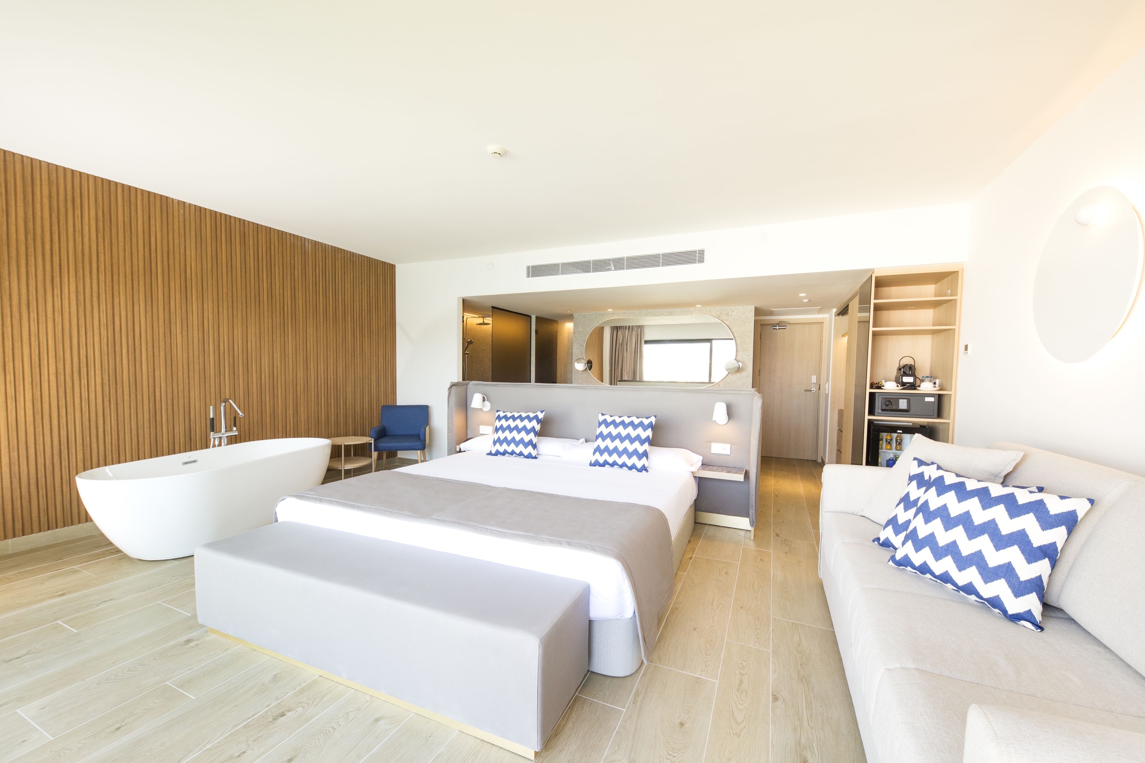 Una habitación de hotel moderna con una cama grande, una bañera, un sofá y una zona de escritorio.