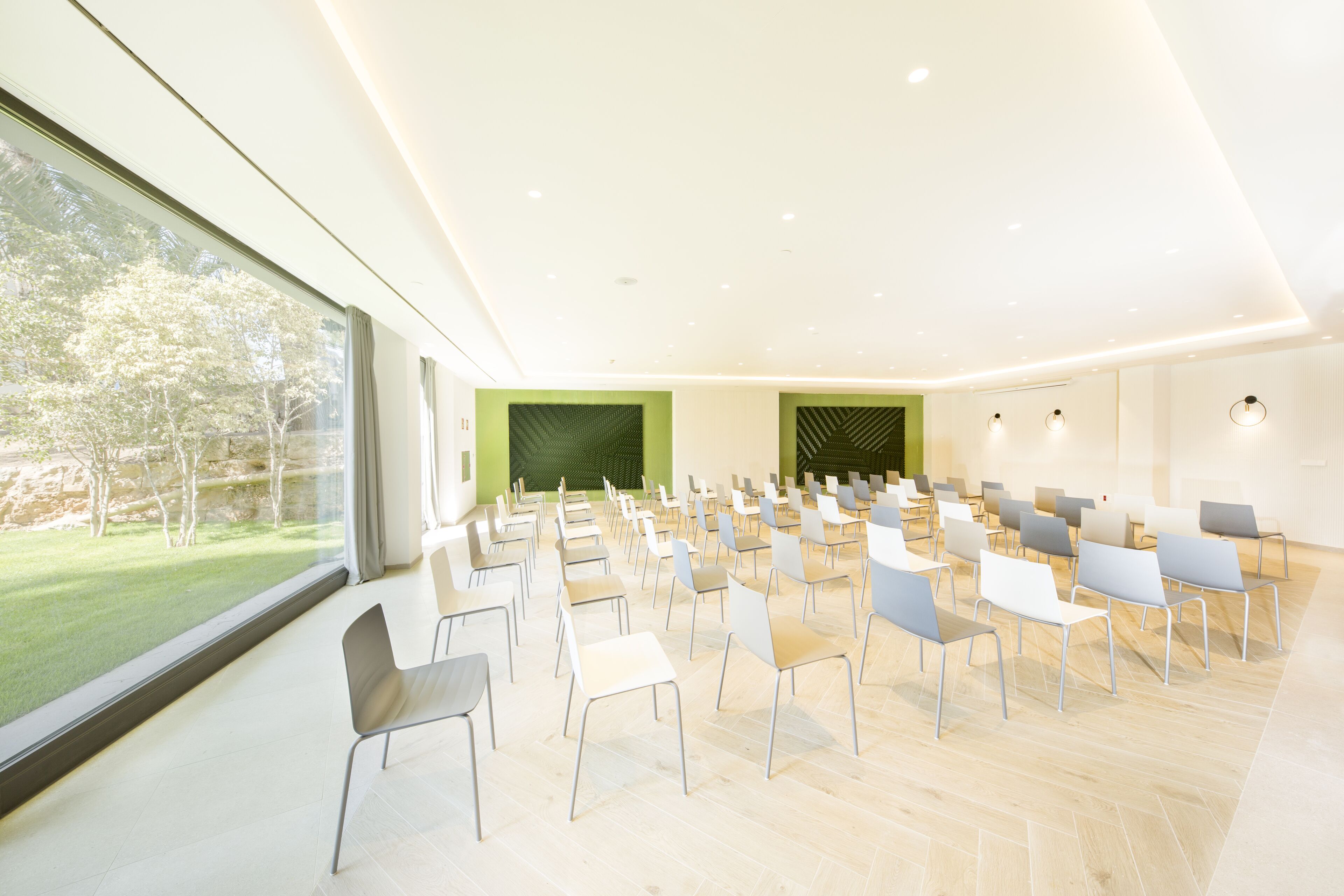 A modern conference room with rows of chairs, large windows, and a green accent wall.