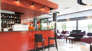 Un espace bar moderne avec un comptoir rouge, des tabourets de bar noirs et un coin salon avec des chaises violettes et noires.