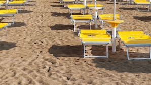 Une plage bordée de rangées de transats et de parasols jaunes, un bâtiment d’hôtel en arrière-plan et un ciel dégagé.