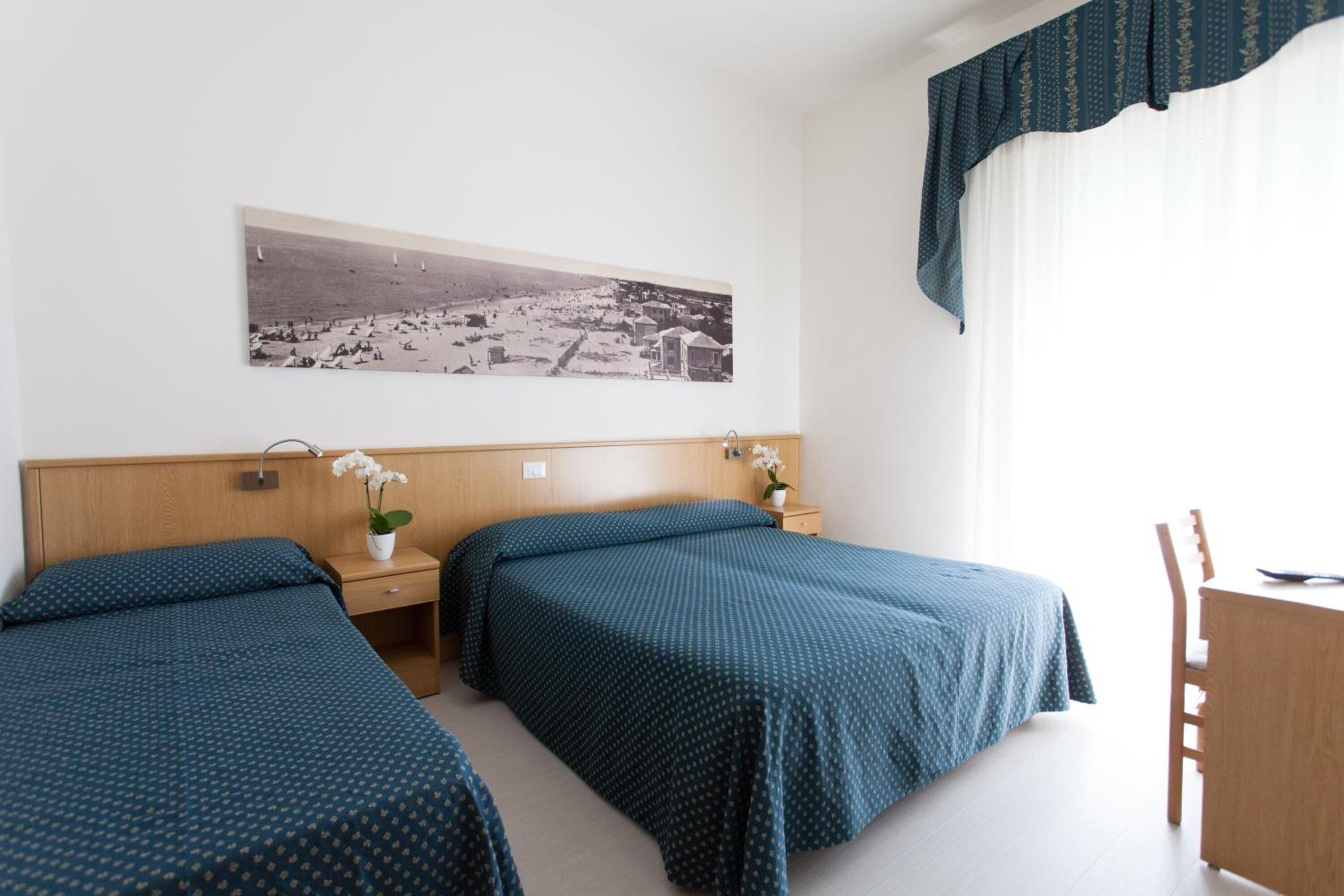 Ett hotellrum med två separata sängar, en sänggavel i trä, ett nattduksbord med en lampa, ett skrivbord och en stol.