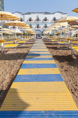 A beachside hotel with a central pathway leading to the entrance, surrounded by rows of beach umbrellas and sun loungers. - Hotel Marina (Jesolo)