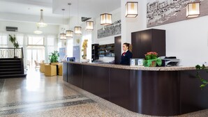 A modern hotel lobby with a curved reception desk, pendant lighting, a large black-and-white photo on the wall, and a staircase leading to the upper floor. - Hotel Marina (Jesolo)