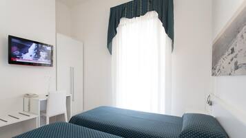 Habitación de hotel con dos camas, un escritorio, una silla, un televisor y una ventana con cortinas.