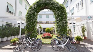 A hotel entrance with a floral archway, bicycles parked in front, and a well-maintained garden. - Hotel Marina (Jesolo)