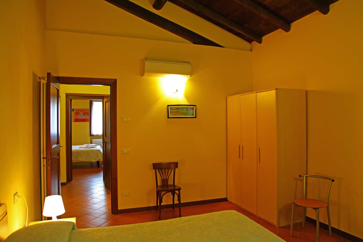 A hotel room with a bed, a chair, a wardrobe, and a door leading to another room.
