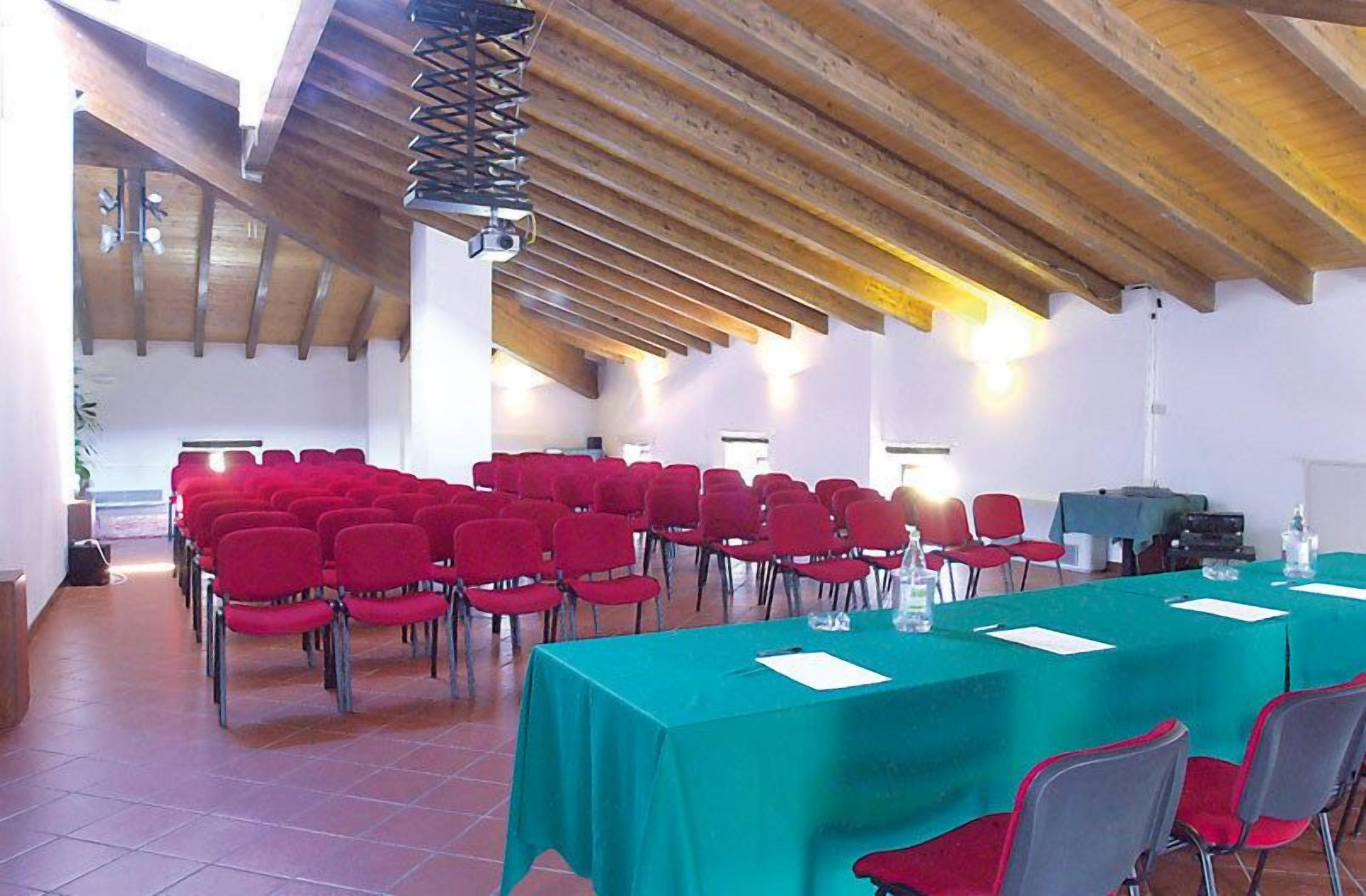 Ein Konferenzraum mit Reihen roter Stühle, einem langen Tisch mit grüner Tischdecke und Holzbalken an der Decke.