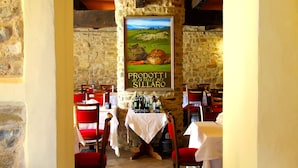 A restaurant interior with stone walls, red chairs, and a table with bottles. - Villaggio della Salute Più (Monterenzio)