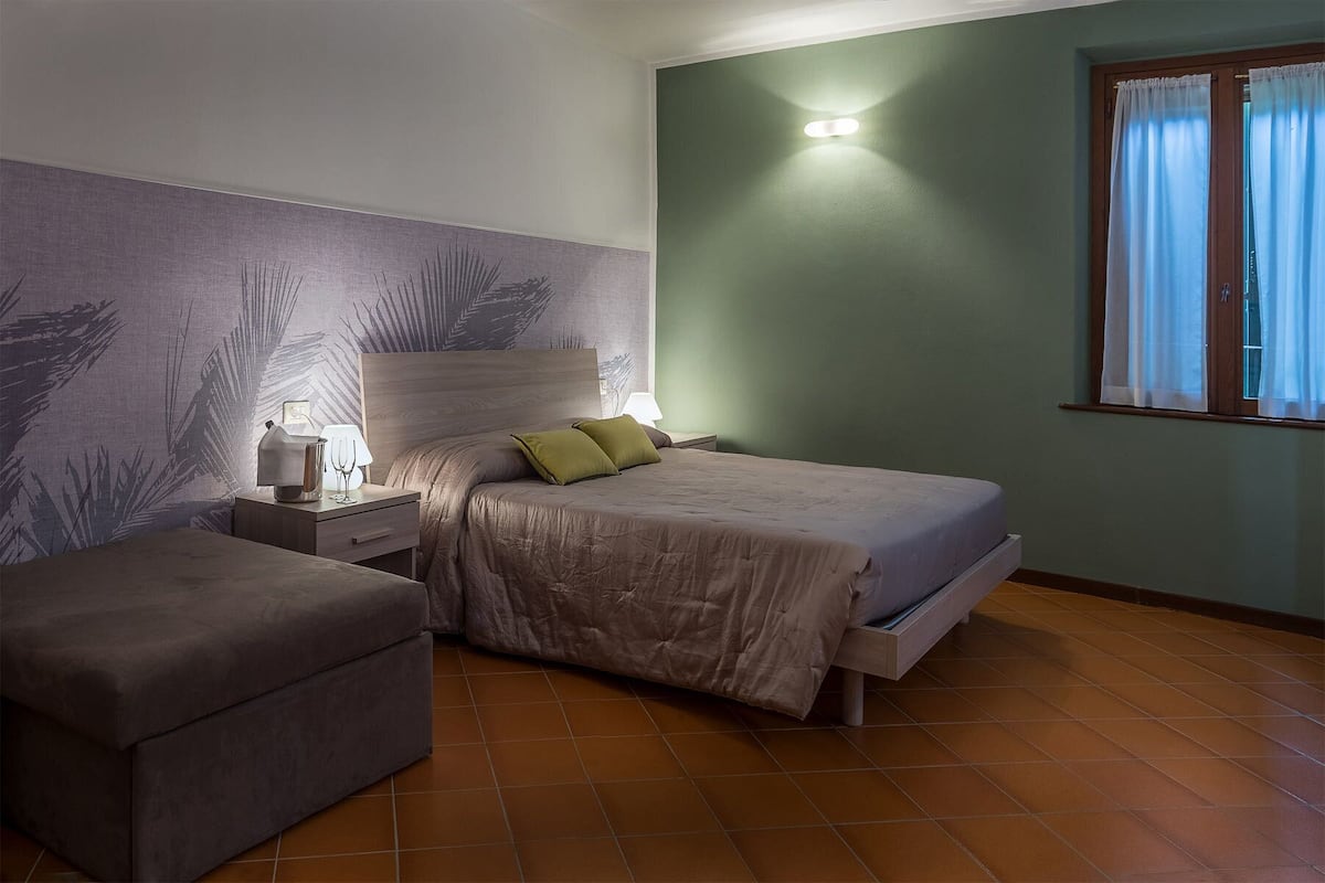 A bedroom with a bed, a nightstand, a lamp, a chair, and a window with curtains.
