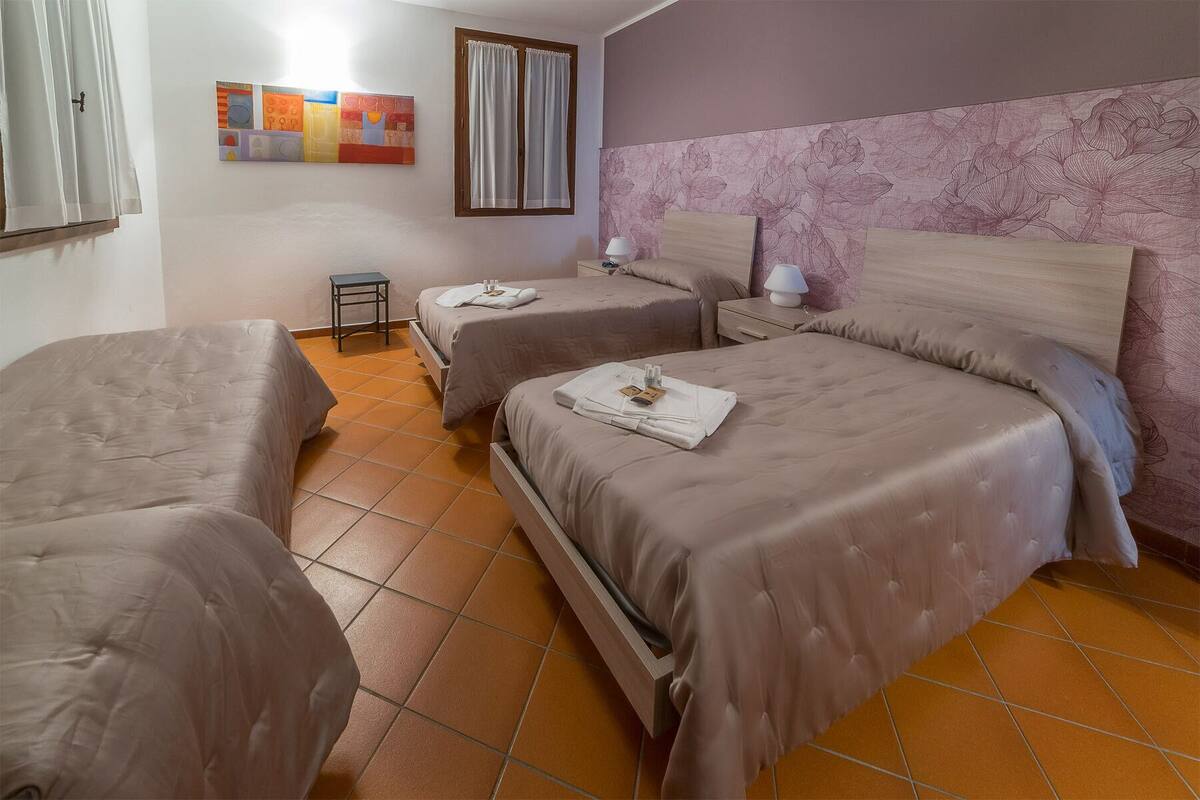 A hotel room with three beds, a small table, and a wall with a floral pattern.