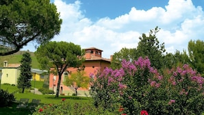 A building with a red roof and a yellow facade, surrounded by green trees and flowering bushes. - Villaggio della Salute Più (Monterenzio)