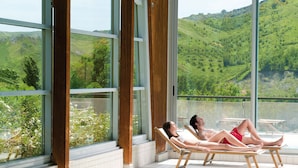 A couple relaxing on sun loungers by a pool with a scenic view of green hills. - Villaggio della Salute Più (Monterenzio)