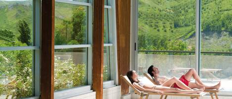 Una pareja descansando en sillones de sol junto a una piscina con una vista panorámica de colinas verdes.