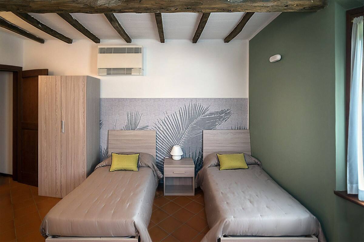 A room with two single beds, a wooden wardrobe, a wall-mounted air conditioner, and a decorative leaf-patterned wall.