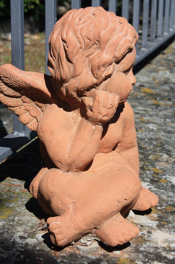 A terracotta statue of a cherub with wings, sitting on a concrete surface. - Villa Sant'Uberto Country Inn (Radda in Chianti)