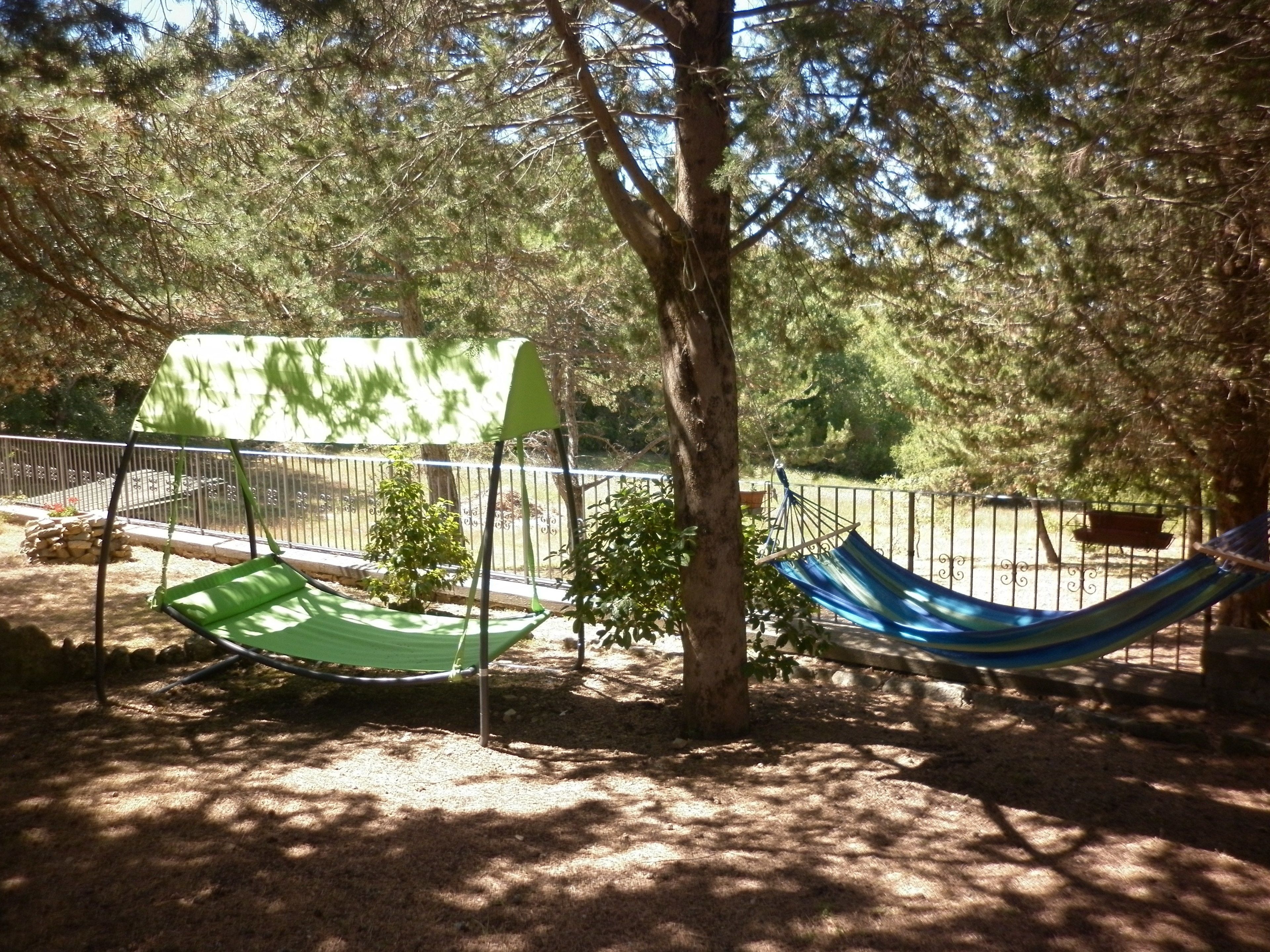 A hammock under a tree in a fenced outdoor area with a stone wall and a bench.
