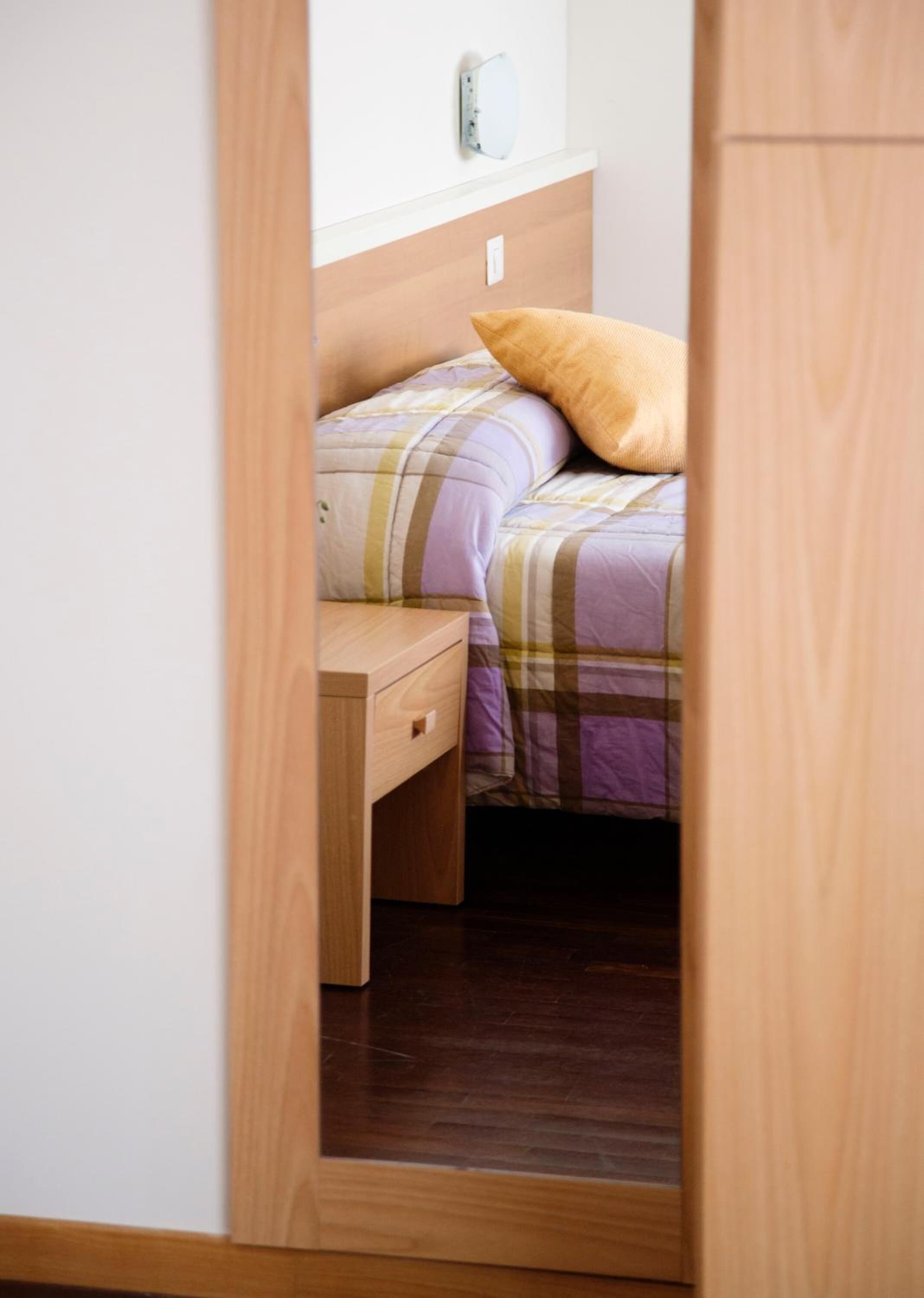 A bedroom with a bed, a nightstand, and a wall-mounted light fixture.
