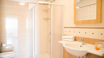 Un baño moderno con ducha de vidrio, lavamanos blanco con espejo superior y un inodoro.
