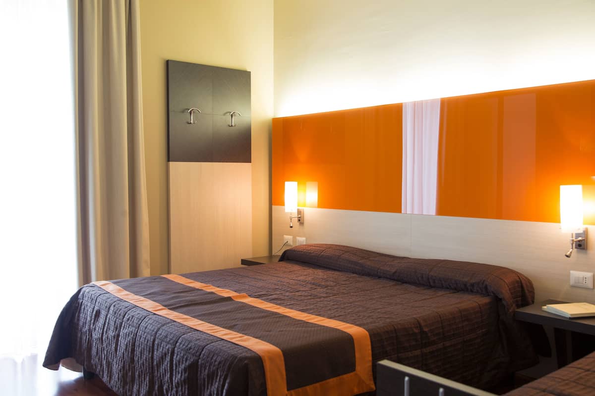 A hotel room with a large bed, two bedside tables, a nightstand, and a wall-mounted light fixture.