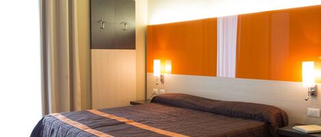 Una habitación de hotel con una cama grande, dos mesitas de noche y una lámpara fijada en la pared.