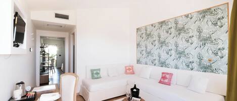 A modern living room with a white sofa, a dining table with a plate of food, and a large floral wallpaper.
