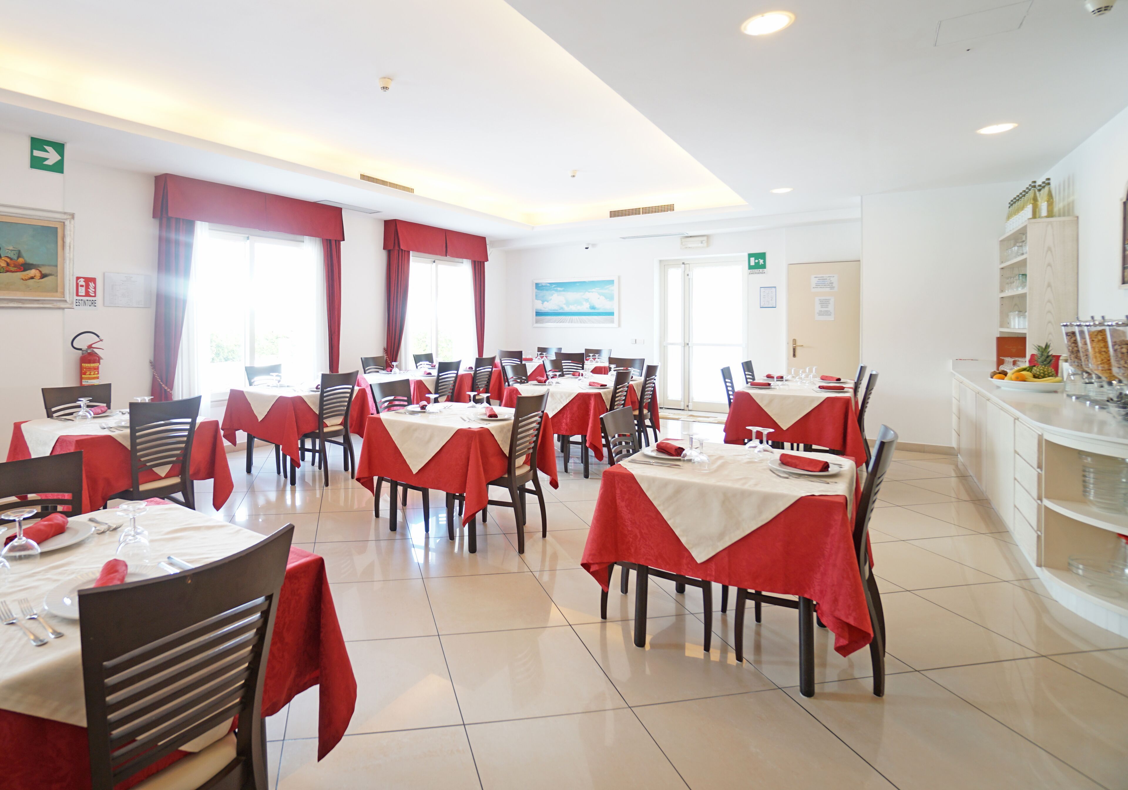A dining area with tables set for multiple people, chairs, and a buffet counter with food items.