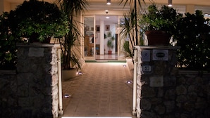 A hotel entrance with a stone pathway leading to a reception area, flanked by potted plants and a sign indicating room number 27. - Hotel Pigalle (Forte dei Marmi)
