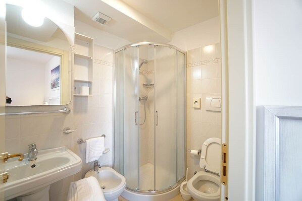 Un baño moderno con ducha de vidrio, lavamanos pedestal, bidé y retrete.