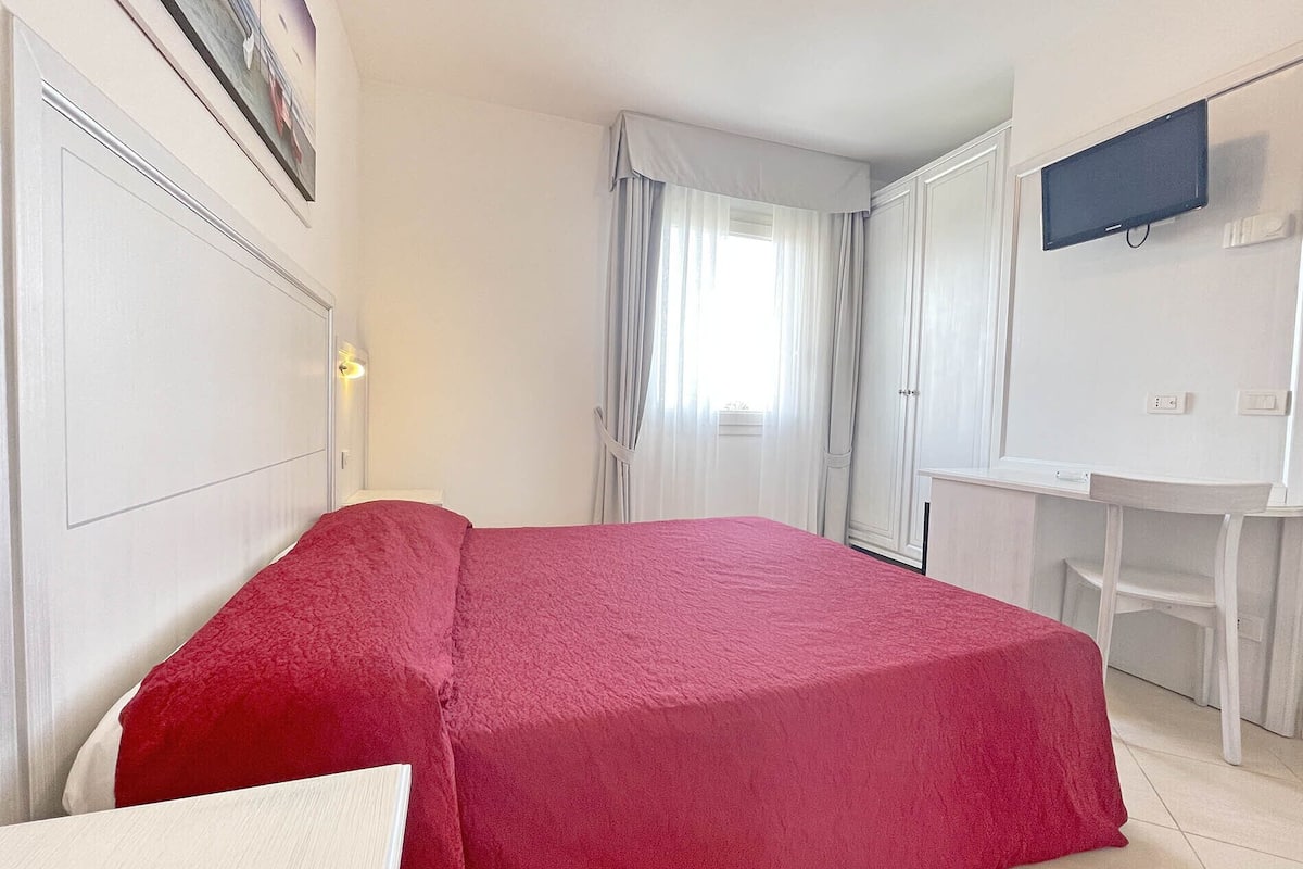 Une chambre d’hôtel avec un lit, un bureau, une télévision et une fenêtre avec des rideaux.