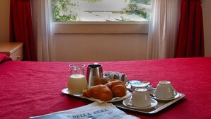 A bed with a red cover, a tray with croissants, a jug of milk, and a cup of coffee. - Hotel Pigalle (Forte dei Marmi)