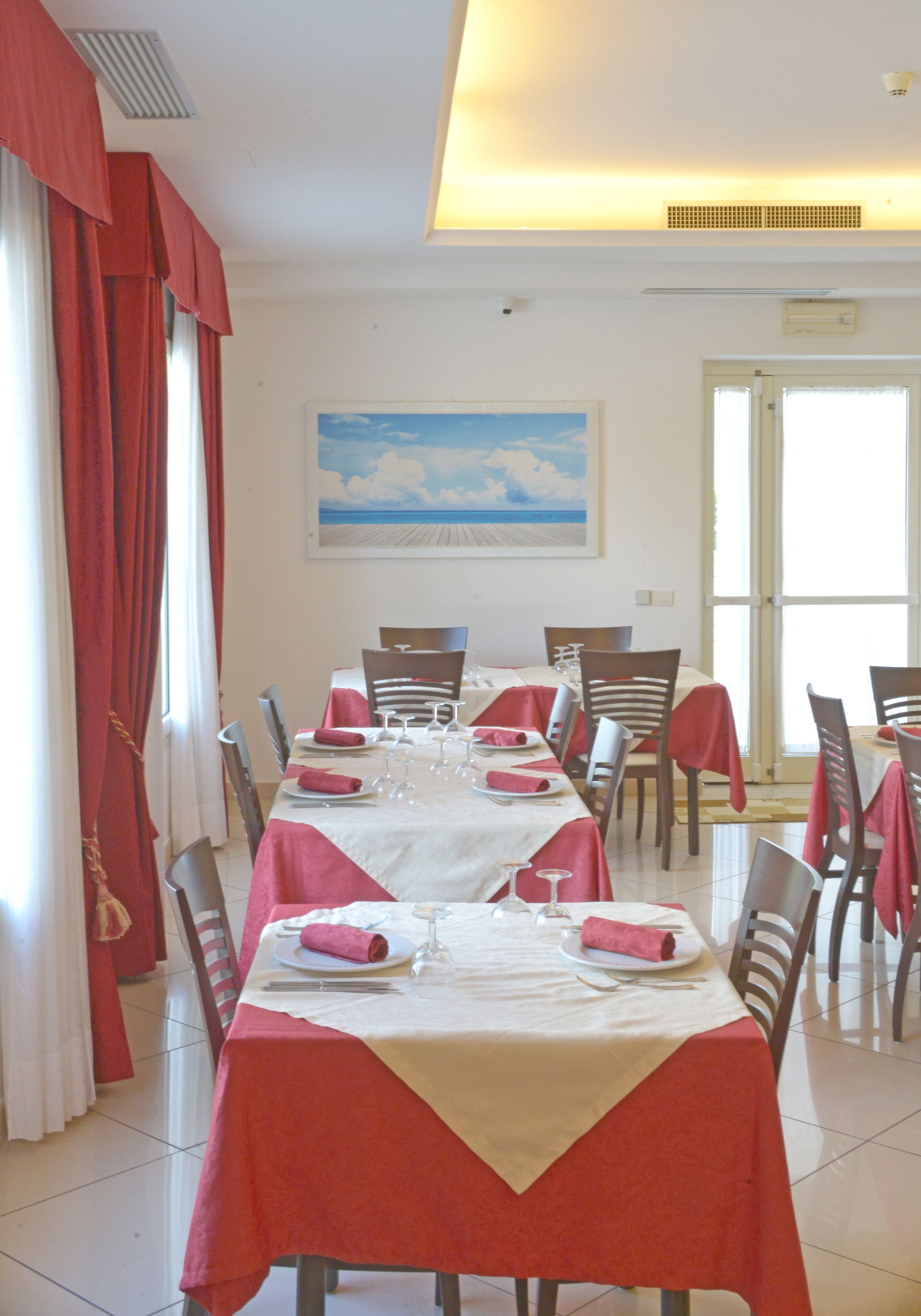 A dining area with a long table set for six, red tablecloths, and chairs.